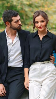 a man and woman sitting next to each other on a bench in front of trees