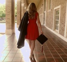 a woman in a red dress is walking down the hall with her purse and coat