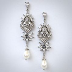 A classy pair of bridal earrings in art deco vintage inspired style. The flawlessly faceted cubic zirconia stones capture the light in a dazzling array of sparkles, while the delicate white pearls add fluidity and motion. The earrings are rhodium / rose gold / yellow gold plated for a bright finish which enhances the intricate detailing and conveys a modern take on old elegance. Length 2.5" (approx. 6.3cm); Width: 0.6" (approx. 1.5cm); Weight: 4.9g Available in Silver, Rose Gold and Yellow Gold Glamorous Wedding Diamond Earrings With Diamond Accents, Glamorous Wedding Diamond Earrings With Accents, Glamorous Cubic Zirconia Pearl Drop Jewelry, Vintage Diamond Pearl Earrings For Wedding, Glamorous Wedding Crystal Earrings With Diamond Accents, Glamorous Diamond Earrings With Elegant Design For Wedding, Elegant Cubic Zirconia Bridal Earrings For Anniversary, Elegant Pearl Earrings With Cubic Zirconia, Glamorous Cubic Zirconia Chandelier Earrings For Anniversary