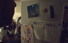 a refrigerator covered in magnets and papers with writing on the door that says get over it