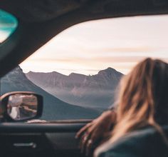 a woman sitting in the passenger seat of a car looking at mountains