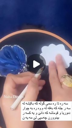 a person writing on a plate with a blue flower in the middle and another hand holding a pencil