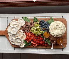 a wooden cutting board topped with fruit and dips on top of a white counter