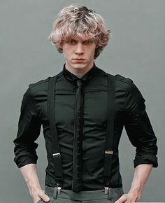 a young man with blonde hair wearing suspenders and a black shirt is standing in front of a gray wall