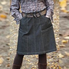 a woman wearing a skirt and boots standing in the leaves with her hands on her hips