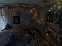 an unmade bed in a bedroom with lights on the wall and pictures above it