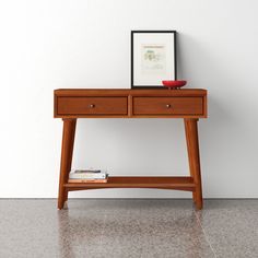 a wooden table with two drawers and a framed photograph on it's top, against a white wall