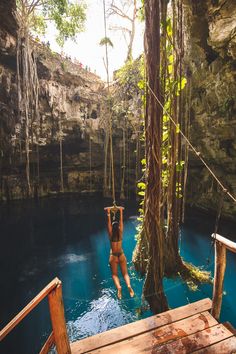 a woman hanging from a rope in the middle of a pool with blue water and trees