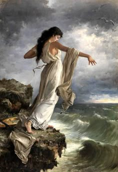 a woman standing on top of a rocky cliff next to the ocean with her arms outstretched