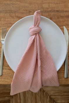 a white plate topped with a pink napkin next to a fork and knife on top of a wooden table