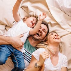 a man, woman and child laying on a bed with their arms in the air