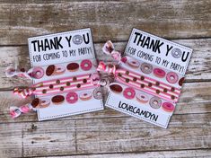 two thank you cards with donuts on them and pink ribbons attached to them, sitting on a wooden surface