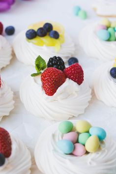 small cupcakes with white frosting and fresh fruit on top, surrounded by candy eggs