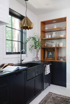 a kitchen with black cabinets and an open book shelf next to the sink in front of a window