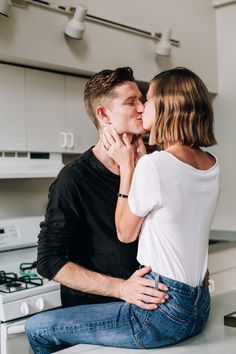 a man and woman sitting on top of a kitchen counter kissing each other's foreheads