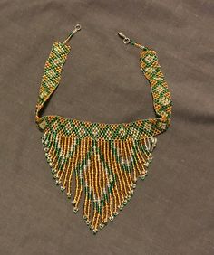 A beautiful gold and green handmade beaded choker style necklace with a beaded bib. This a unique, one-of-a-kind piece! This is a handmade piece of African Beadwork jewelry, directing benefitting the maker of the jewelry, the Chigamba family of the Zona tribe in Zimbabwe and EMERGE. These styles are not only for good, they are truly beautiful statement pieces that will wow anyone. This necklace is one-of-a-kind meaning it is unique to the maker. If the original necklace is sold - you may buy a c African Style Necklace, African Beadwork, Kind Meaning, Black Gold Necklace, Beadwork Jewelry, Tiered Necklace, Original Necklace, Beadwork Necklace, Choker Style Necklace