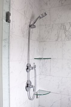 a shower head with glass shelves on the side and marble tile wall behind it in a bathroom