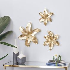 three gold metal flowers on a white wall next to a vase and bookends