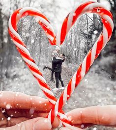 a person holding a candy cane in the shape of a heart with snow falling on them