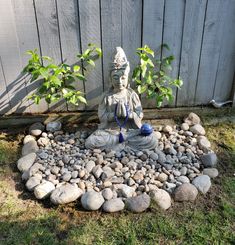 a buddha statue sitting on top of a pile of rocks next to a small tree