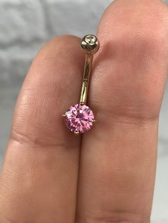 a close up of a person's hand holding a ring with a pink diamond