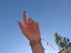 a person's hand holding up the peace sign in front of a blue sky