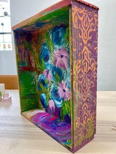 a colorful box sitting on top of a wooden table next to a vase filled with flowers