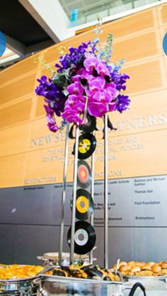 there is a tall vase with purple flowers on top of it and vinyl records in the bottom