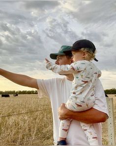 a man holding a small child in his arms while standing on top of a field