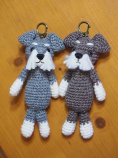 two crocheted stuffed animals are sitting on a wooden table, one is gray and the other is white