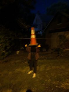 a person standing in the grass with a traffic cone on their head at night time