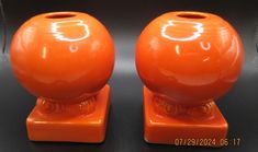 two orange vases sitting on top of a black table next to eachother