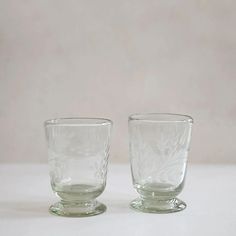 two clear glass cups sitting next to each other on a white tableclothed surface