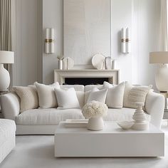 a living room filled with white furniture and pillows on top of a table in front of a fire place