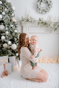 a woman holding a baby in front of a christmas tree