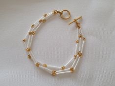 This classy bracelet is made with three strands of silver lined white opal Delicas on links of gold plated wire. It is finished with a gold plated toggle clasp and measures 7.5 inches long. White Multi-strand Bracelet As Gift, White Multi-strand Beaded Bracelets As Gift, Handmade White Beaded Metal Bracelets, Handmade White Beaded Metal Bracelet, White Wire Wrapped Bracelets For Jewelry Making, White Multi-strand Beaded Bracelets, White Multi-strand Bracelets For Jewelry Making, Double Strand White Beaded Bracelets, White Beaded Double Strand Bracelet