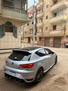 a silver car parked on the side of a road in front of some tall buildings