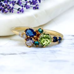 two rings with different colored stones sitting on top of a marble table next to lavender flowers