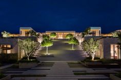 the entrance to a modern home at night with trees and bushes on either side of the walkway