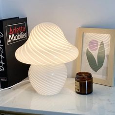 a white lamp sitting on top of a table next to a framed photo and a candle