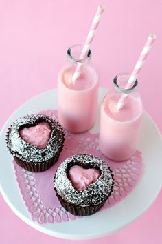 three cupcakes on a plate with two cups of milk