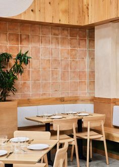 an empty restaurant with wooden tables and white plates on the table, next to a potted plant