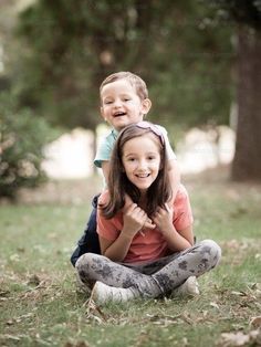 two children are sitting on the ground and one is holding onto the other's back