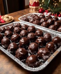 two trays of chocolate truffles on a table with christmas decorations in the background