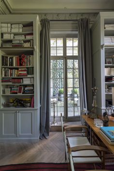 a living room filled with furniture and bookshelves next to a window covered in curtains