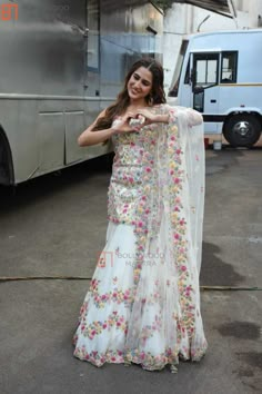 a woman standing in front of a bus wearing a white dress with flowers on it