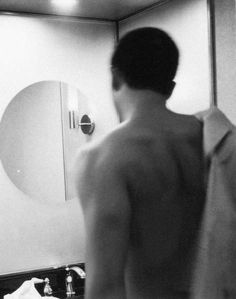 a shirtless man standing in front of a bathroom mirror looking at himself in the mirror