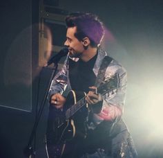 a man with purple hair playing an acoustic guitar in front of a microphone on stage