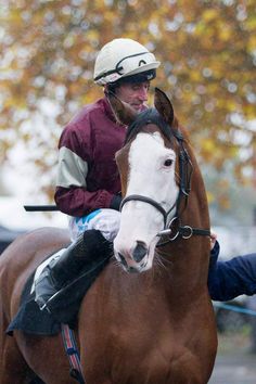 a man riding on the back of a brown horse next to a person wearing a helmet