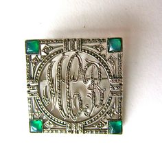 a brooch with the letter g on it's side and green stones in the middle